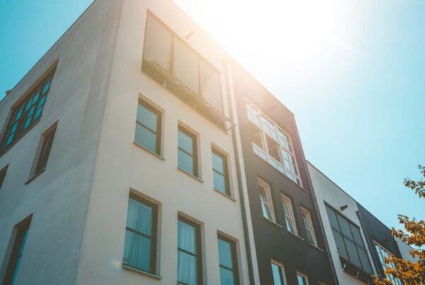 Condo Building Insurance - Angled View Looking up at a White and Black Colored Modern Condo Building with Sunlight Shining and Reflecting on Windows at Dusk